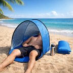 Orange pop-up beach tent with UV protection set up on sandy beach, showing full structure with carry bag alongside