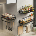 Black aluminium wall-mount kitchen shelf with integrated hooks holding spice bottles and utensils