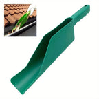 Green plastic gutter cleaning scoop used by gloved hand to remove wet leaves from a residential roof gutter