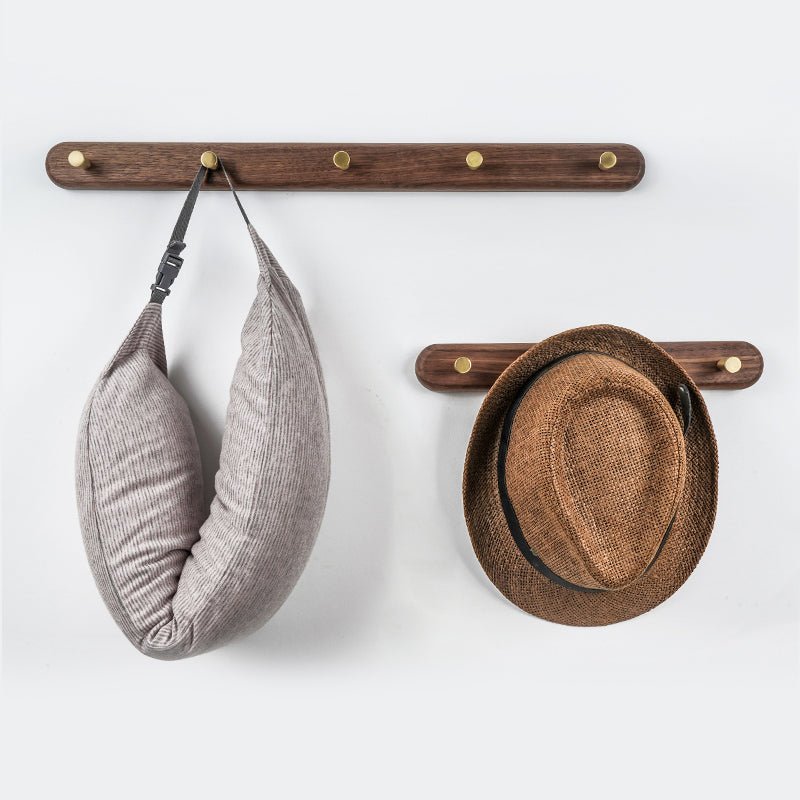 Walnut wood wall coat rack with five brass knob hooks mounted on a white wall, coat and hat hanging