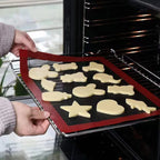 Silicone baking mat black mesh with red border being placed onto oven wire rack with shaped biscuits on top