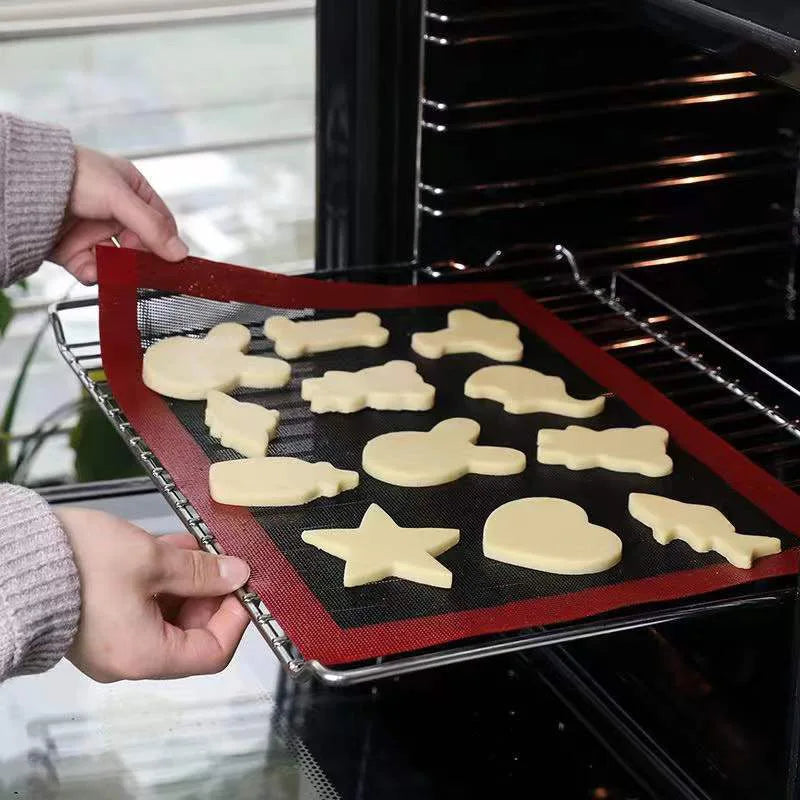 Silicone baking mat black mesh with red border being placed onto oven wire rack with shaped biscuits on top