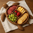 Wooden turtle serving board with five sections filled with crackers, cheese, grapes, strawberries and salami on linen napkin