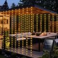Solar LED curtain lights warm white draped over garden pergola at dusk with solar panel visible in foreground