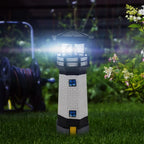 Solar lighthouse garden light LED rotating beam illuminated at night amongst garden flowers