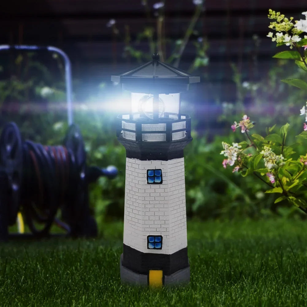 Solar lighthouse garden light LED rotating beam illuminated at night amongst garden flowers