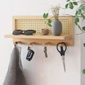 Wooden wall shelf with rattan back panel and four hooks mounted in hallway, keys and cloth hanging, vase on top ledge