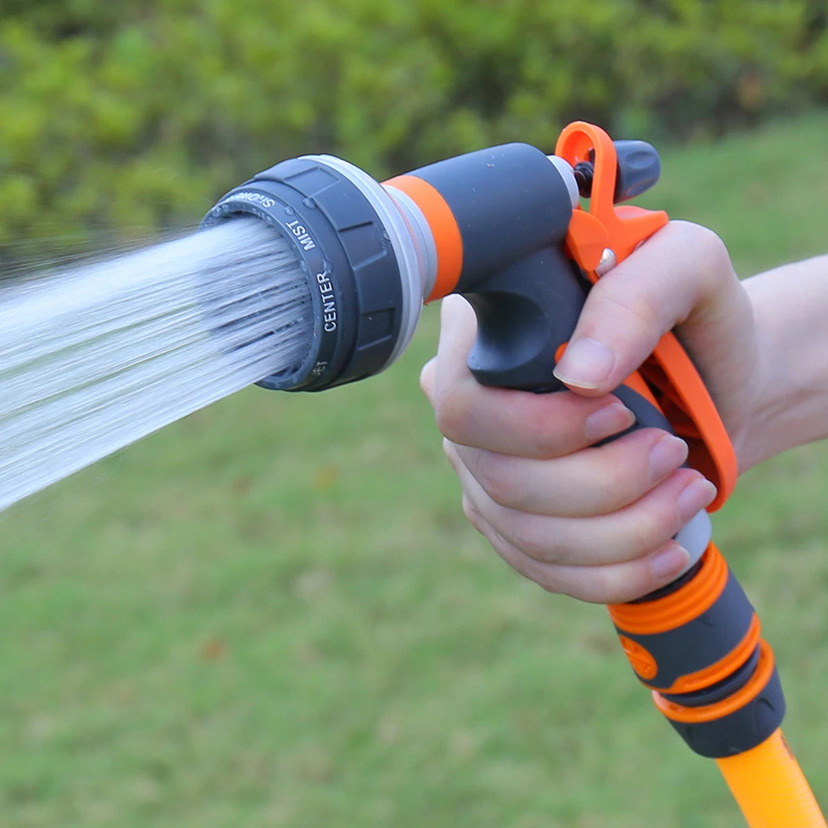 Garden spray gun orange black ABS plastic being used outdoors showing water spray pattern