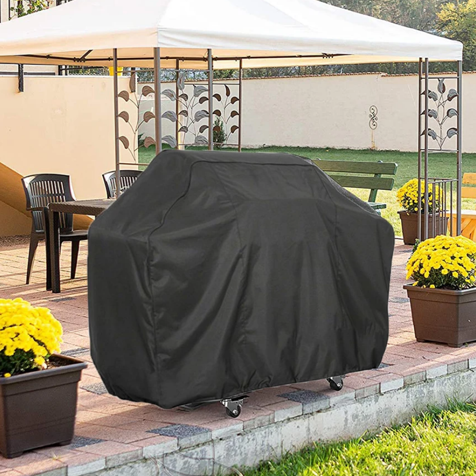 Black waterproof BBQ cover fitted over a freestanding trolley barbecue on an outdoor patio, front three-quarter view