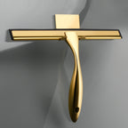 Gold shower squeegee with rubber blade hanging on wall-mount hook inside modern tiled bathroom, front view