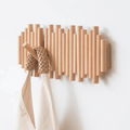 Wooden wall coat rack with staggered cylindrical rods and folding hooks, mounted in a light AU hallway with linen jacket hanging