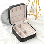 Black travel jewellery box open showing cream interior ring rolls and earring slots in lid, styled on white linen bedside surface