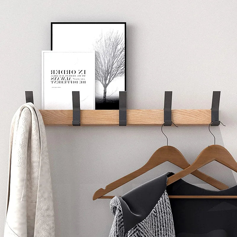 Wall-mounted wooden coat rack with black metal hooks holding coats and hangers in a hallway setting