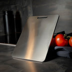 Steel cutting board with non-porous surface on dark kitchen bench with red tomatoes
