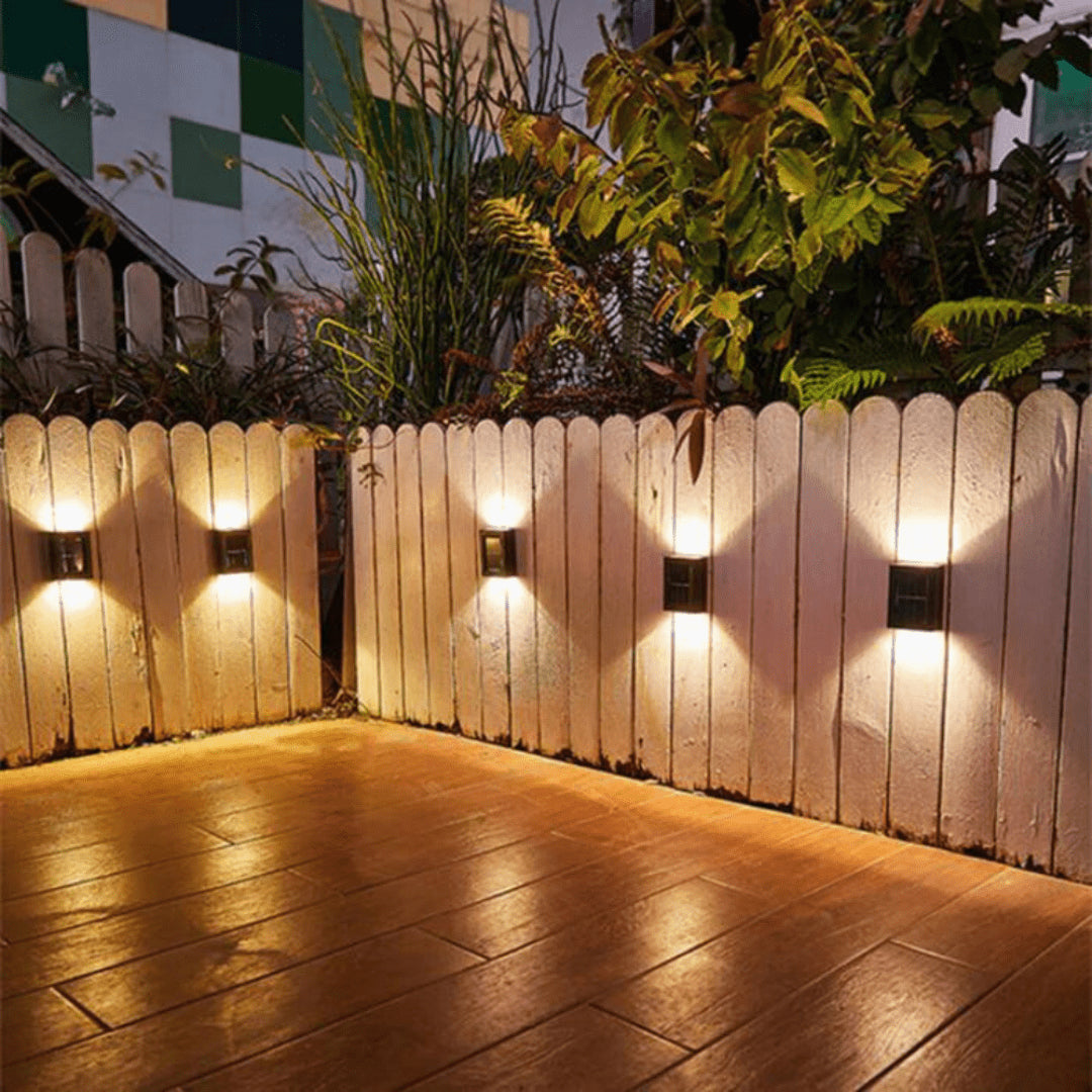 Solar fence lights with warm LED illumination mounted on wooden garden fence at night