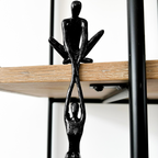 Black resin abstract connected souls sculpture with two intertwined figures, displayed on a natural wooden shelf in a lounge room setting