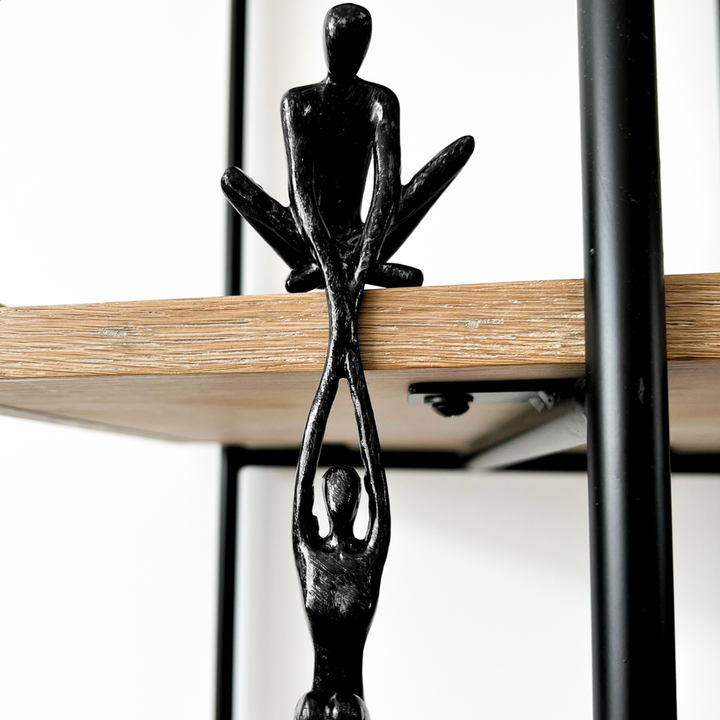 Black resin abstract connected souls sculpture with two intertwined figures, displayed on a natural wooden shelf in a lounge room setting