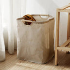 Foldable beige cotton-linen laundry basket with wooden handles on timber floor in bright bedroom lifestyle setting