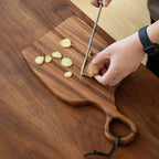 Hands slicing fresh ginger on walnut cutting board kitchen prep lifestyle shot