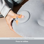 Hand pressing the circular valve on a grey inflatable camping pillow to demonstrate the inflation mechanism