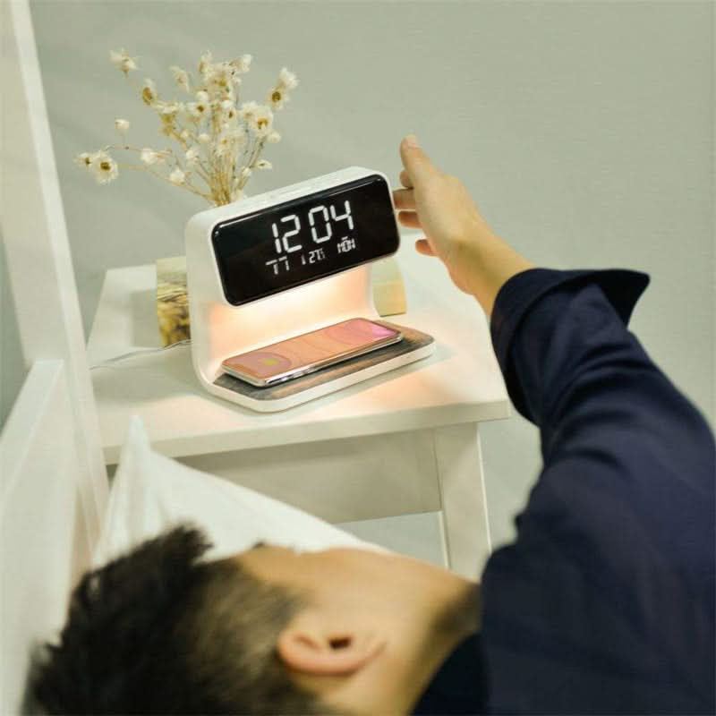 Hand touching dimmer controls on white bedside lamp with phone charging wirelessly on pad