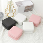 Three travel jewellery boxes in Black White and Pink colours closed on white textured background with gold wire vase in background