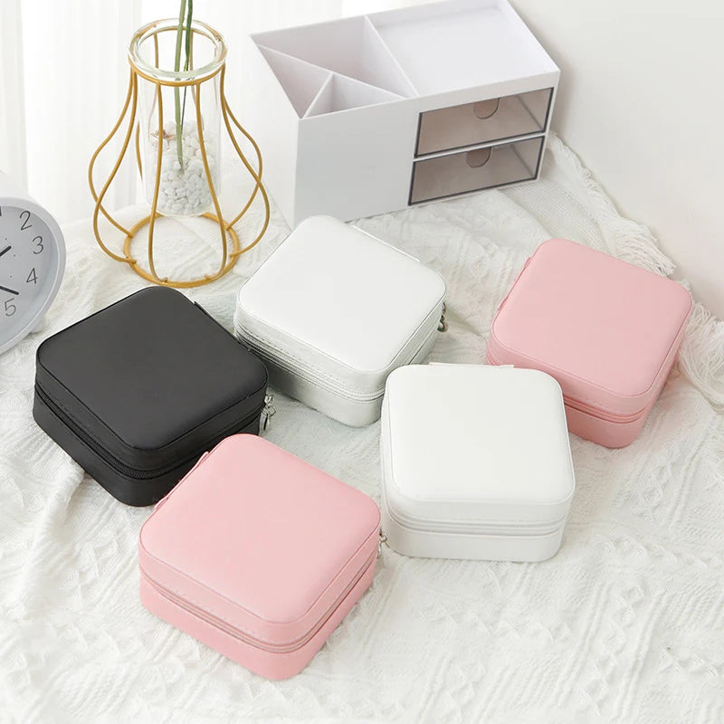 Three travel jewellery boxes in Black White and Pink colours closed on white textured background with gold wire vase in background