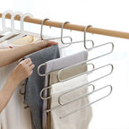 Hand placing grey striped trousers onto a 5-layer stainless steel pants hanger on a wooden wardrobe rod