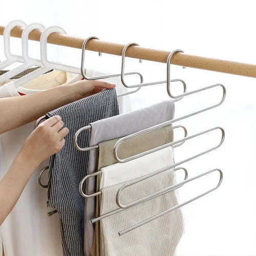 Hand placing grey striped trousers onto a 5-layer stainless steel pants hanger on a wooden wardrobe rod