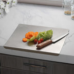 Hands cutting vegetables on stainless steel board with edge hooked over kitchen benchtop