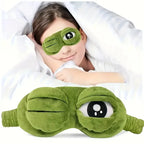 Woman lying in white bed wearing green 3D frog face sleep mask looking relaxed against white pillows