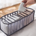 Hand placing a rolled sock into a grey 7-grid nylon mesh drawer organiser in a bright room setting