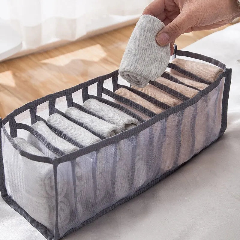 Hand placing a rolled sock into a grey 7-grid nylon mesh drawer organiser in a bright room setting