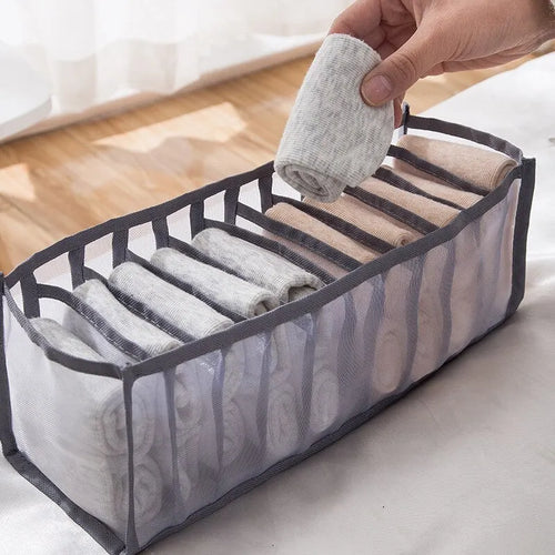 Hand placing a rolled sock into a grey 7-grid nylon mesh drawer organiser in a bright room setting