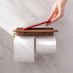 Double roll walnut wood toilet roll holder with gold frame, hand placing red phone on wooden shelf top