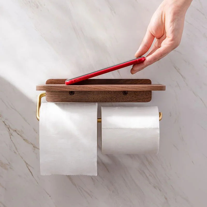 Double roll walnut wood toilet roll holder with gold frame, hand placing red phone on wooden shelf top