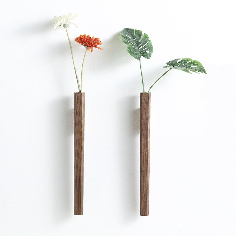 Walnut wood wall vase holding orange gerbera daisy on white wall with framed art and books in background