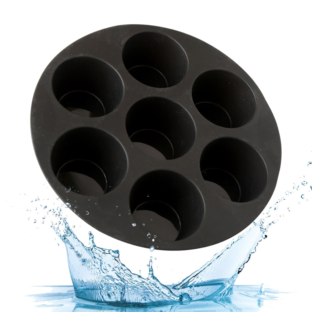 Silicone muffin mould loaded with seven egg tarts inside open green air fryer basket on kitchen bench