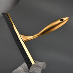Gold shower squeegee on wall hook beside bathroom mirror, styled with white towels and ceramic soap dish