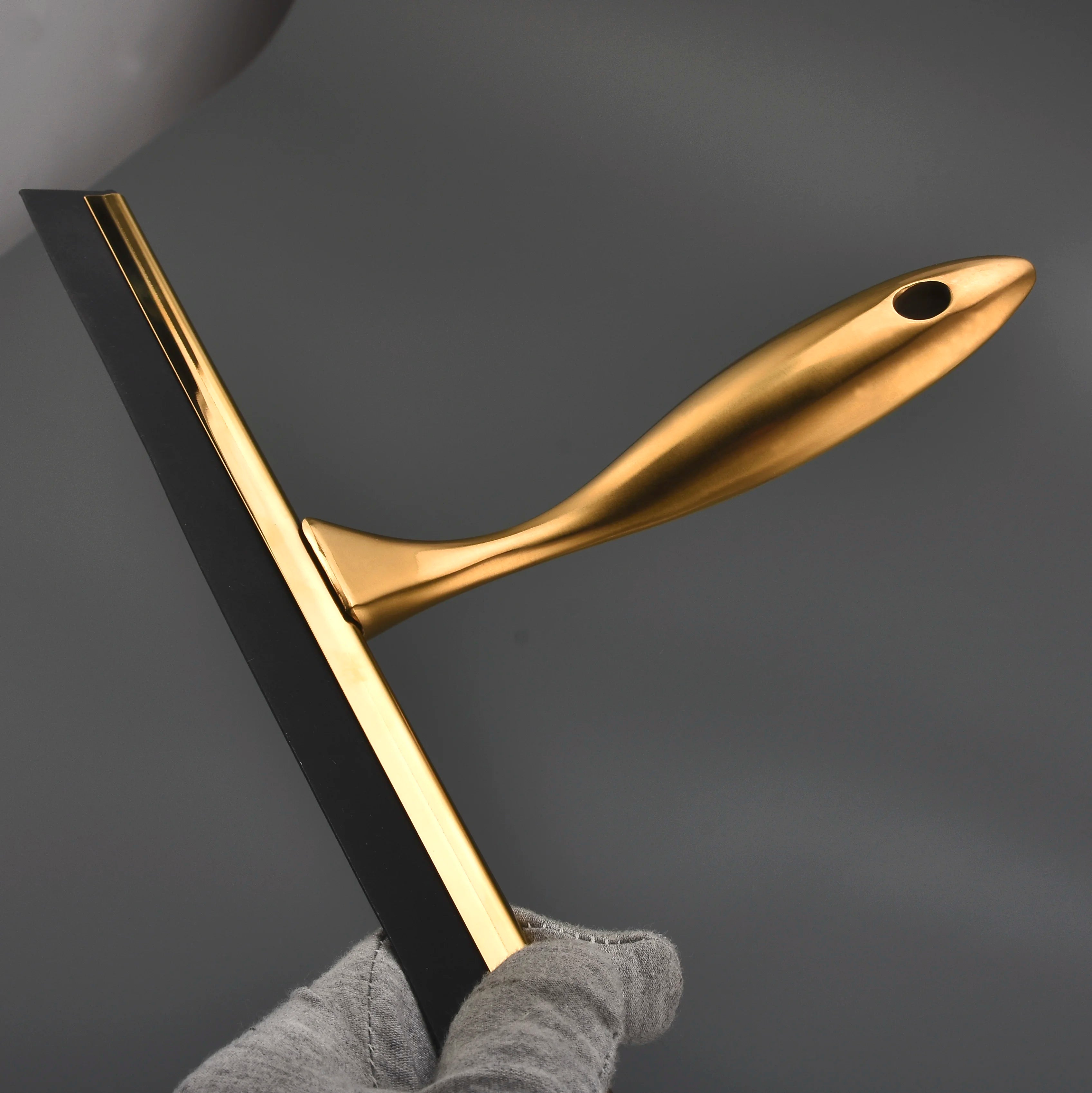Gold shower squeegee on wall hook beside bathroom mirror, styled with white towels and ceramic soap dish