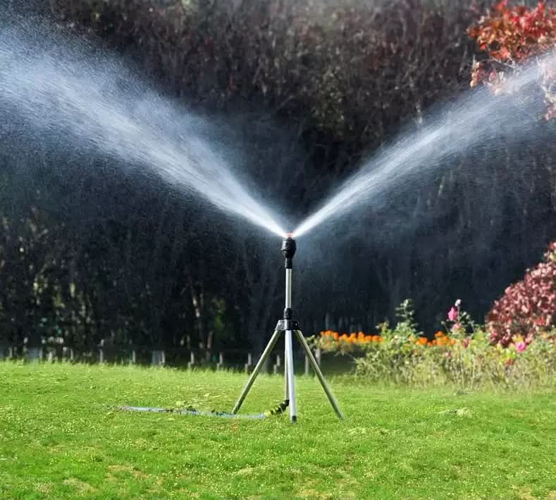 Close-up view of adjustable sprinkler head mechanism and tripod connection on grass surface