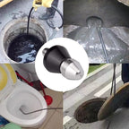 Hand holding stainless steel high-pressure nozzle over blocked outdoor drain with water stream visible in garden setting