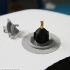 Hand connecting SUP pump adapter to inflatable board valve outdoors at waterside in natural daylight