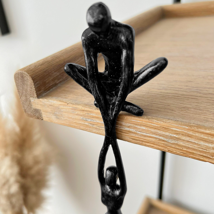 Black abstract two-figure resin sculpture on a white studio background showing full silhouette and sculptural form from slight angle
