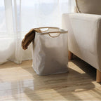 Close-up of smooth wooden carry handle on natural beige cotton-linen laundry basket showing texture detail