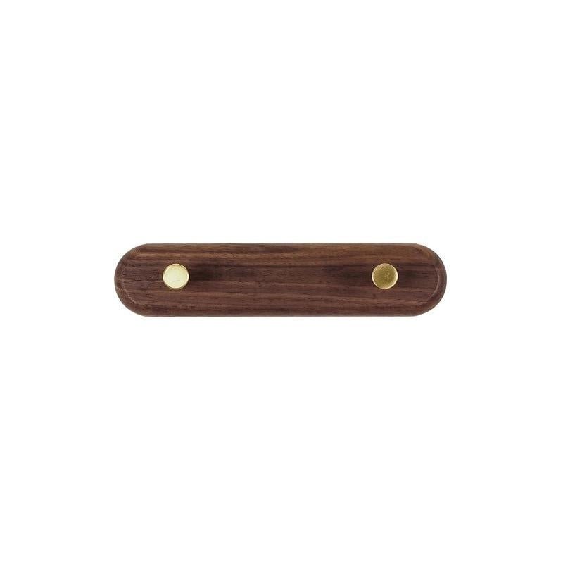 Close-up of brass knob hook on walnut wood coat rack rail showing smooth wood grain and brass finish