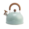 Three stovetop whistling kettles in white, light green, and black arranged on natural timber surface, colour variant overview