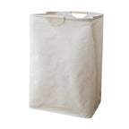 Hands placing folded clothing into open beige cotton-linen laundry basket in a bedroom setting